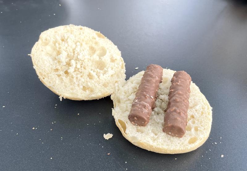 Een opengesneden kaiserbolletje met daarin een doormidden gebroken branchli.