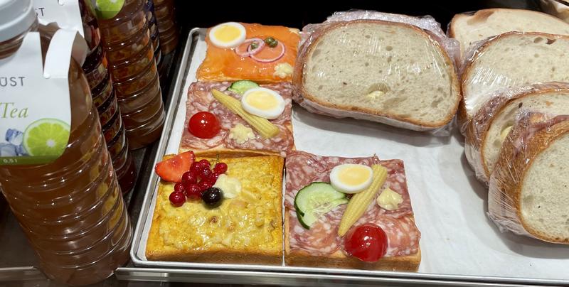 Vier belegde boterhammen met verschillende toppings, waaronder zalm, ei, tomaat, komkommer en bessen, naast een stapel gesneden brood.