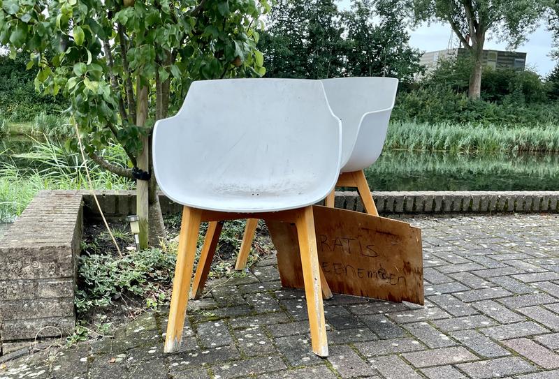 Twee witte kuipstoelen op een oprit met een bordje 