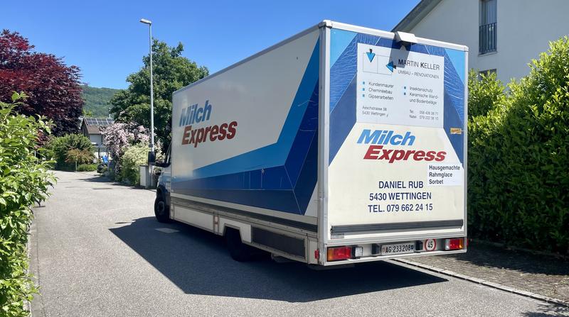 Vrachtwagen van Milch Express geparkeerd op een straat, met contactinformatie en bedrijfslogo op de achterkant.