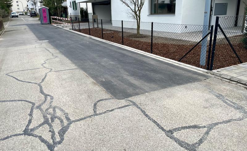 Een asfaltstraat voor een nieuw gebouwd huis. Scheuren in het wegdek zijn opgevuld met teer en een verse strook asfalt van 10 bij 1 meter ligt voor het huis.